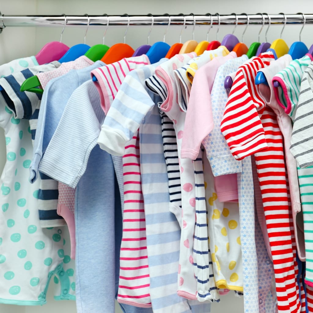 A row of colorful baby and kids' clothing hanging on a rack, with many items made from lightweight, soft chambray fabric.