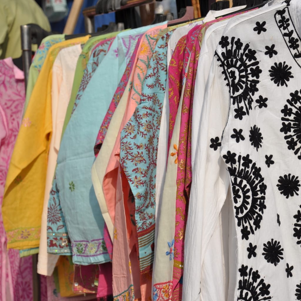 A colorful display of various embroidered and patterned fabrics hanging on a rack, including silk and chiffon materials in vibrant colors and intricate designs.