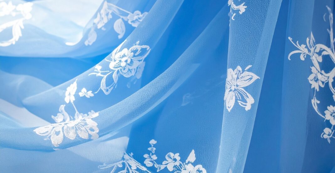 A close-up of a sheer blue fabric with white floral embroidery.