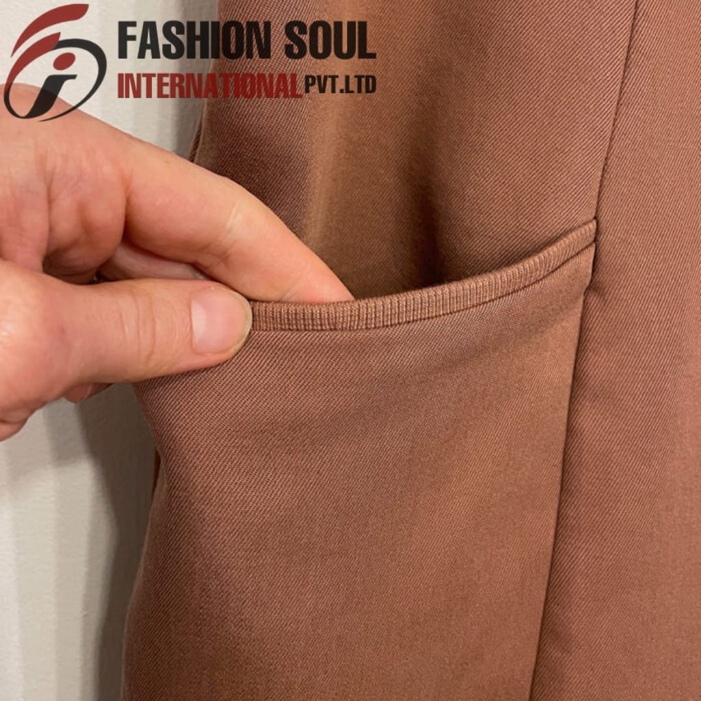Close-up of a hand holding the pocket of a brown fabric garment, showing the neat stitching and texture of the material.