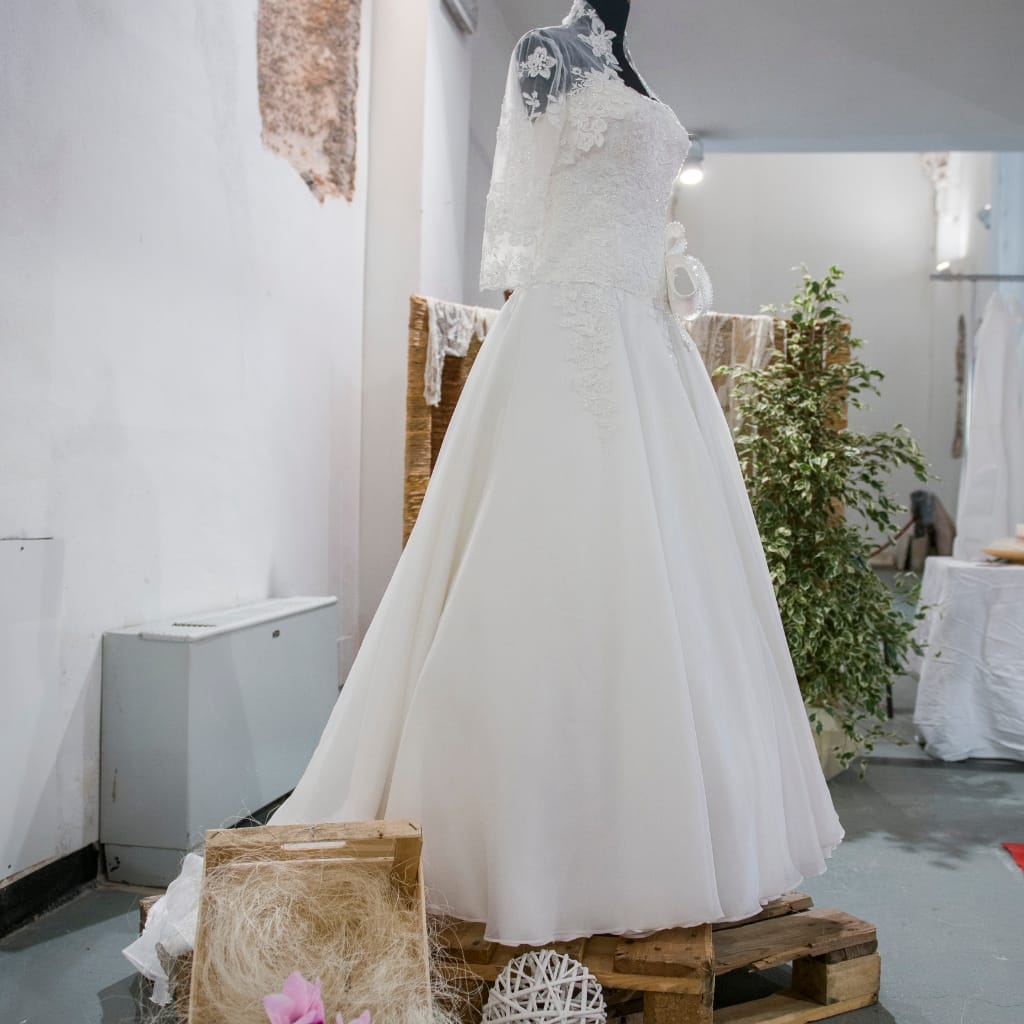 Close-up of a wedding gown made from pure chiffon fabric, featuring delicate lace detailing on the bodice and sleeves, displayed on a mannequin in a bridal boutique.