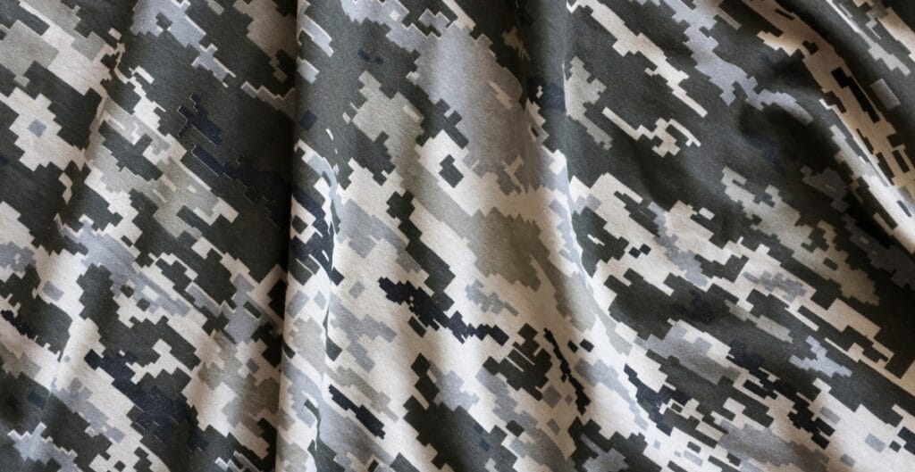 A close-up image of a fabric with a digital camouflage pattern in shades of gray, black, and beige.