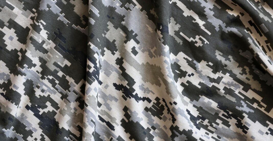 A close-up image of a fabric with a digital camouflage pattern in shades of gray, black, and beige.