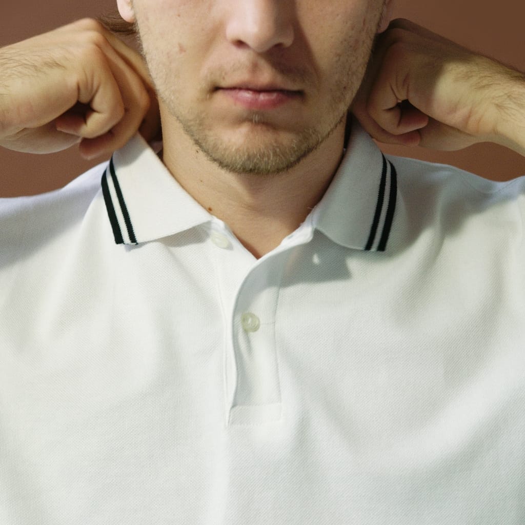 Close-up of a man adjusting his white polo shirt with a black striped collar.