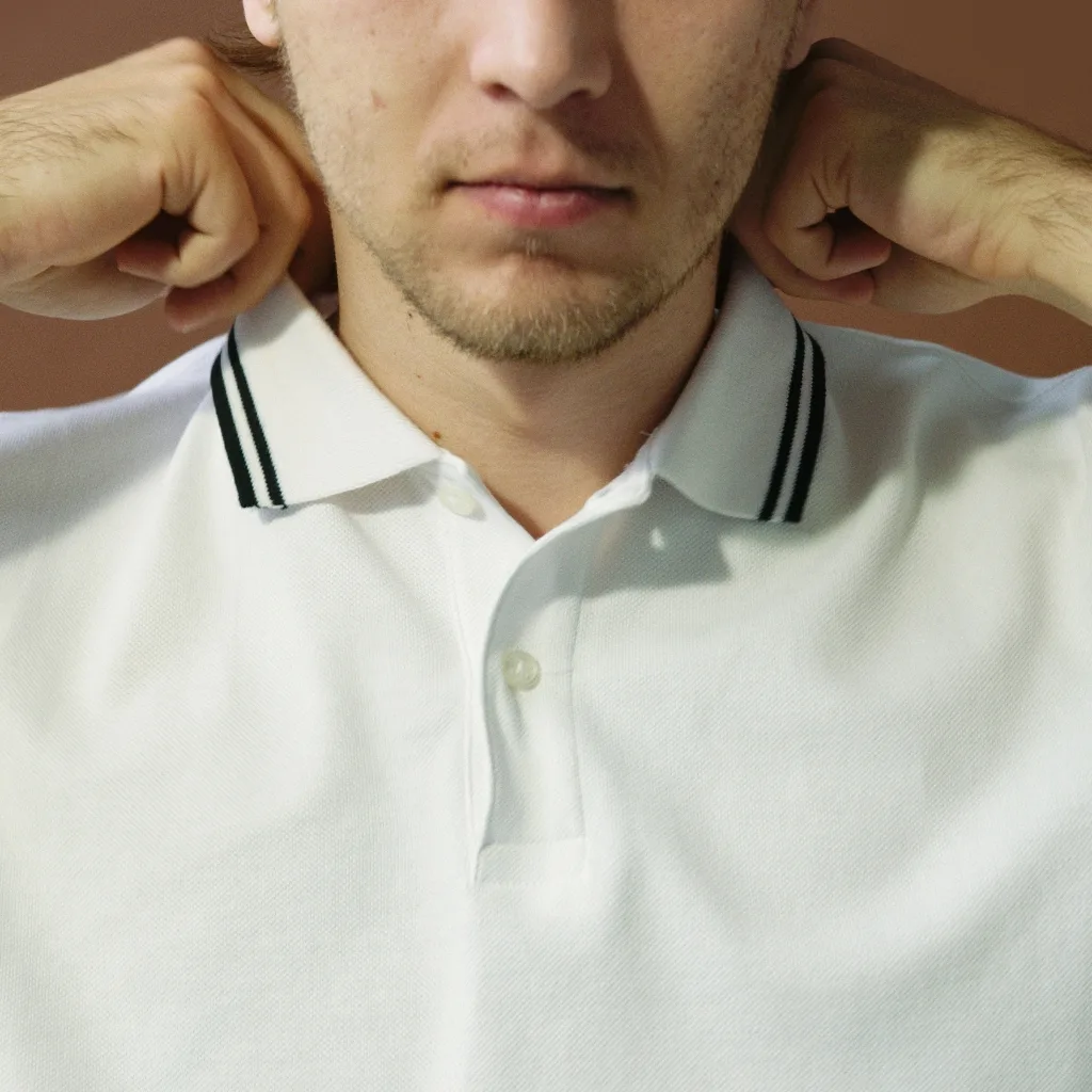 Close-up of a man adjusting his white polo shirt with a black striped collar.