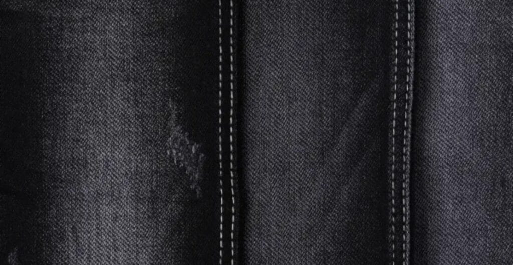 Close-up of black denim fabric with subtle texture, showing tight weave and tiny white specks, highlighting the fabric’s rich color.