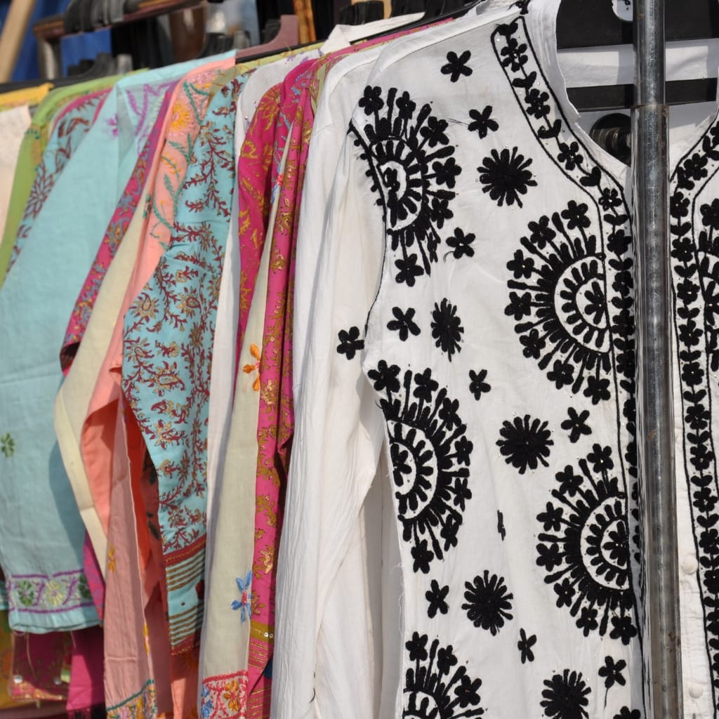 A row of colorful embroidered cotton and spandex garments hanging on a rack, showcasing various patterns and designs, including floral and intricate embroidery.