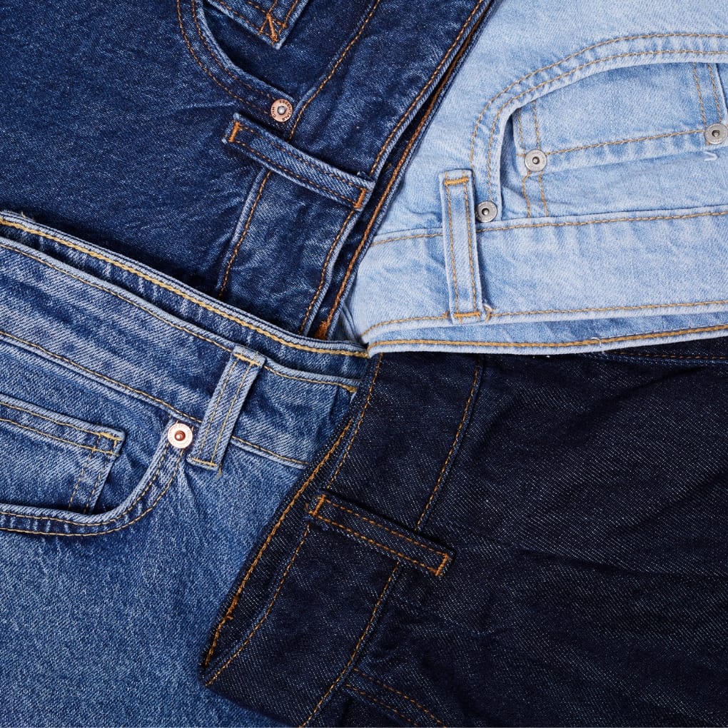 Close-up of four stacked pairs of jeans in various shades of blue, arranged to showcase different denim textures and stitching details.