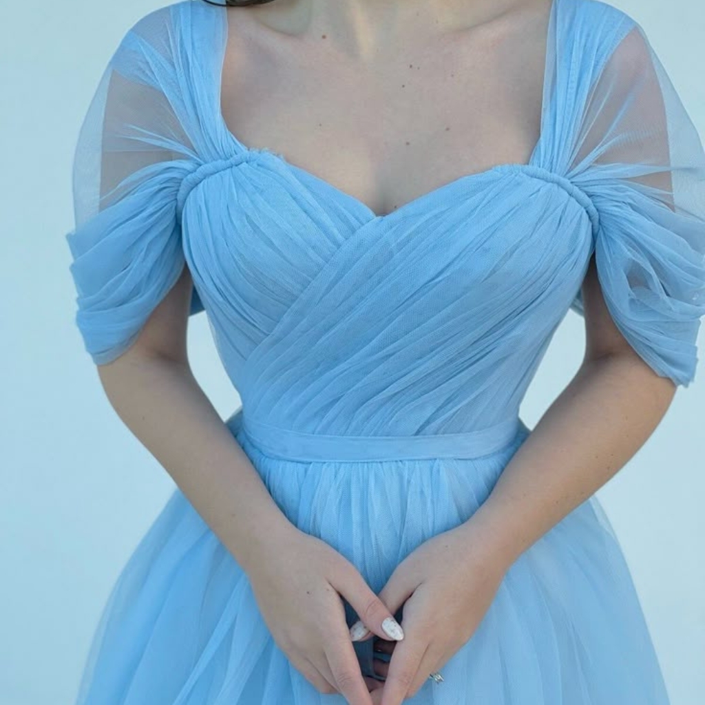 Close-up of a woman wearing a light blue tulle dress with puffed sleeves, her hands gently clasped in front of her.