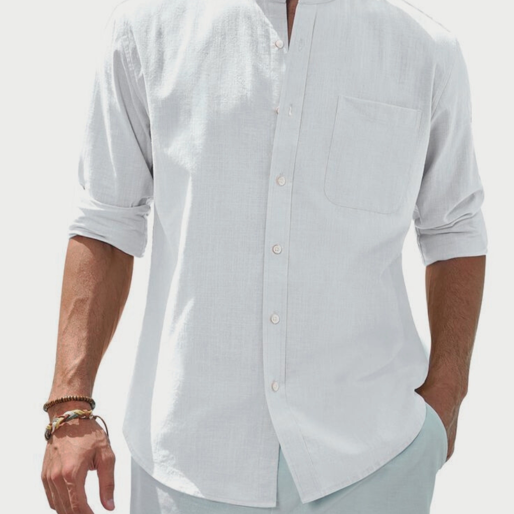 A person wearing a white, long-sleeved cotton button-down shirt with the sleeves rolled up. The shirt features a chest pocket and is paired with light-colored pants.
