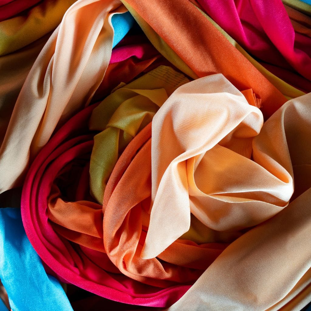Close-up image of multicolored satin weave cotton fabric with smooth, shiny, and silky texture, featuring shades of peach, pink, green, beige, and blue.