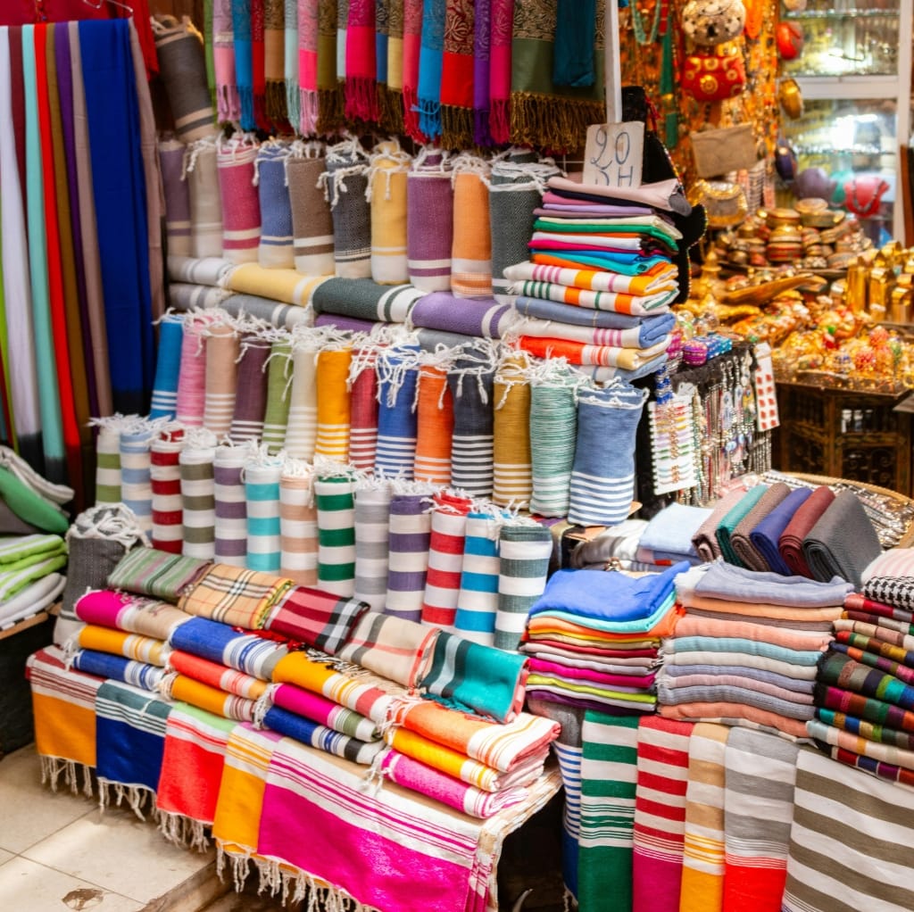 Colorful display of various folded and rolled textiles, including brushed cotton fabrics, at a market stall.