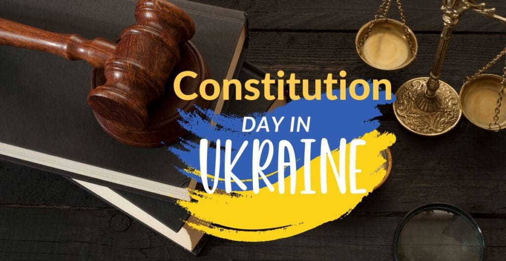 A gavel, a book, a pair of scales, and a magnifying glass arranged on a dark wooden surface with an overlay of the Ukrainian flag colors (blue and yellow) and the text "Constitution Day in Ukraine."