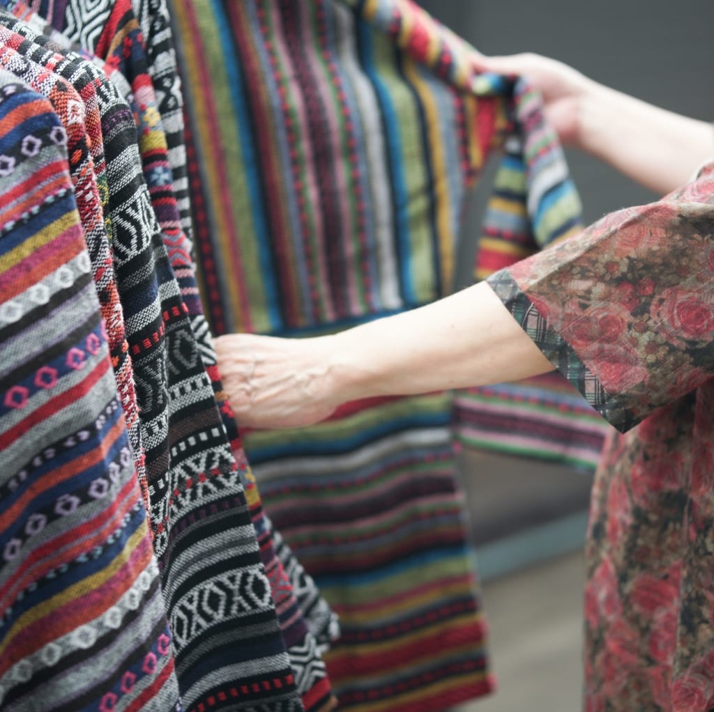 Close-up of hands touching and inspecting vibrant, woven cloth with colorful, intricate patterns, highlighting the fabric's texture and craftsmanship.