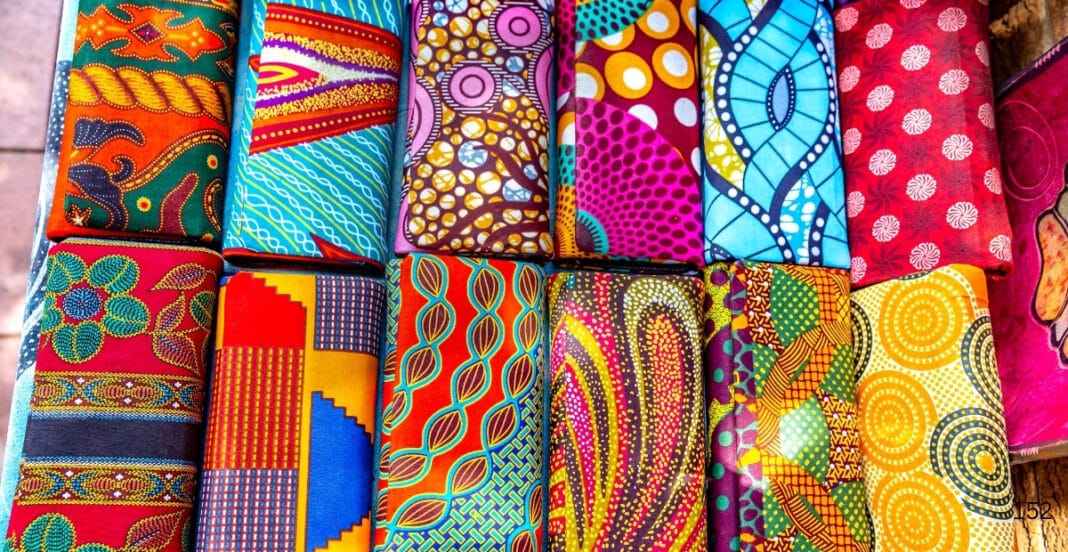A colorful display of various printed fabric rolls featuring vibrant patterns and designs, arranged in a grid-like pattern.
