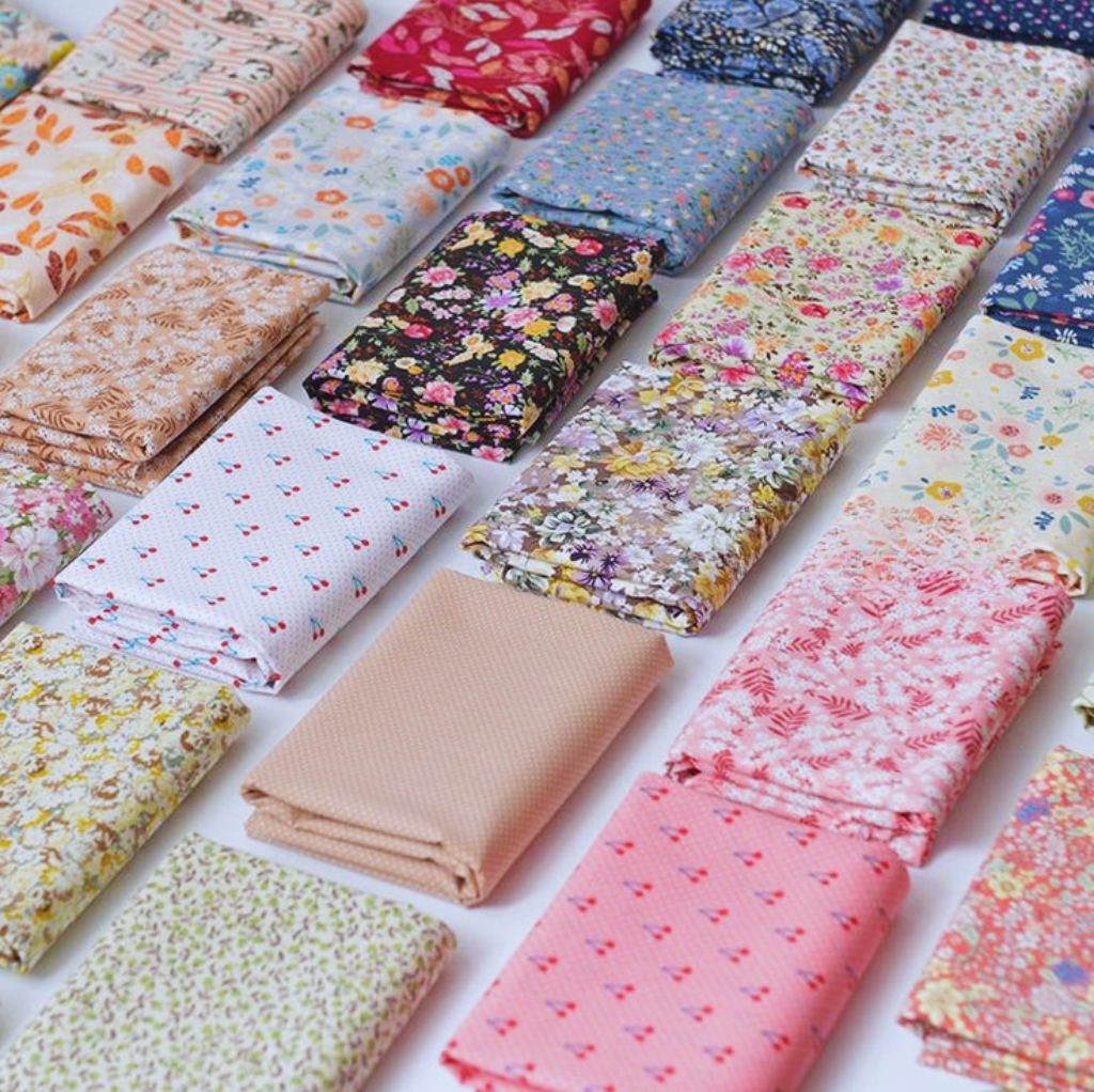 A display of multiple folded cotton print fabrics with various colorful floral and pattern designs, neatly arranged in rows.