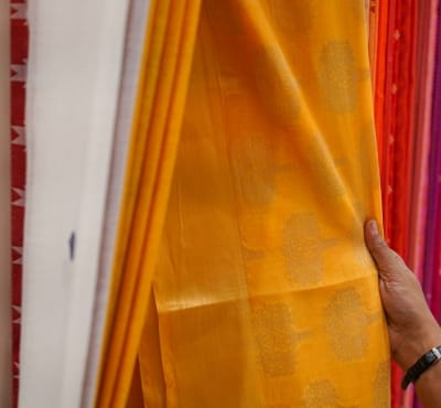 A hand holding a piece of orange cotton silk fabric on a display rack in a fabric store.
