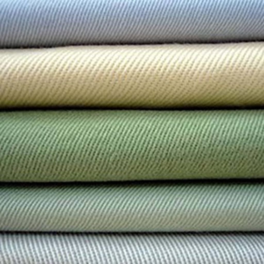 Stacked rolls of fabric in various shades of light green, beige, and gray.