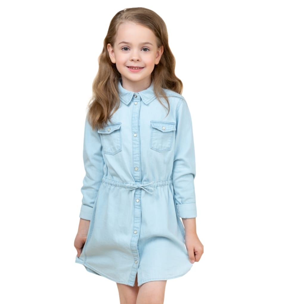 A young girl with long, wavy light brown hair, smiling softly, wearing a light blue denim chambray dress with rolled sleeves and button details, standing against a white background.