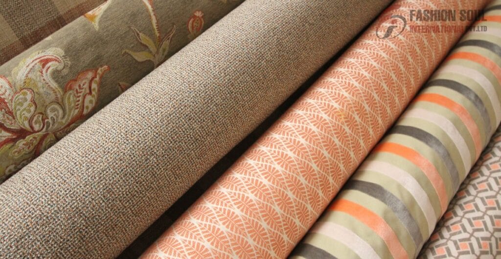 Rolls of patterned fabric with floral, textured, leaf, and geometric designs in neutral, orange, and pastel shades.