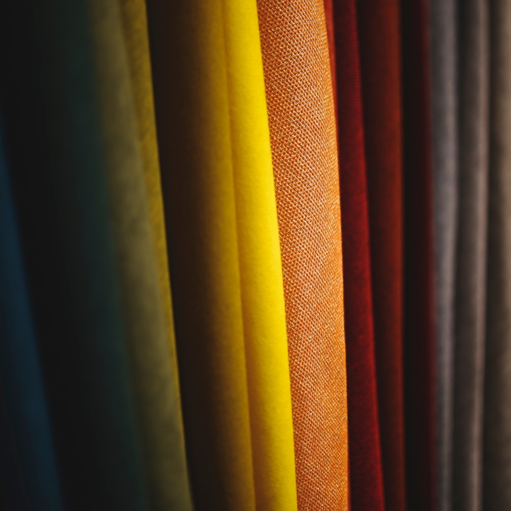 Close-up of colorful fabric rolls arranged vertically, featuring shades from dark green, yellow, orange, red, to dark gray.