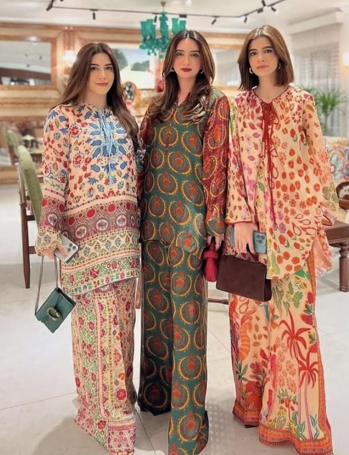 Three women standing indoors, wearing colorful, patterned cotton print fabrics in traditional and contemporary styles.