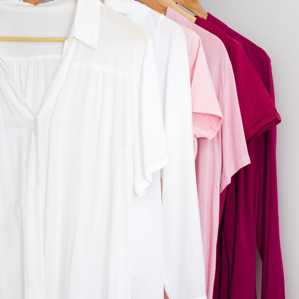 A row of women's blouses hanging on hangers, featuring white, light pink, and deep magenta colors.