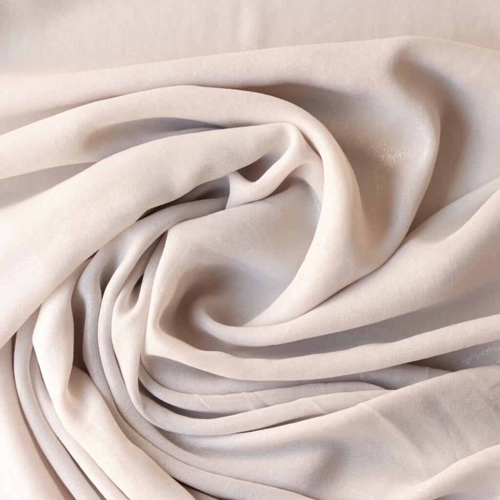 Close-up of soft, flowing, cream-colored fabric with gentle folds and subtle shimmer.
