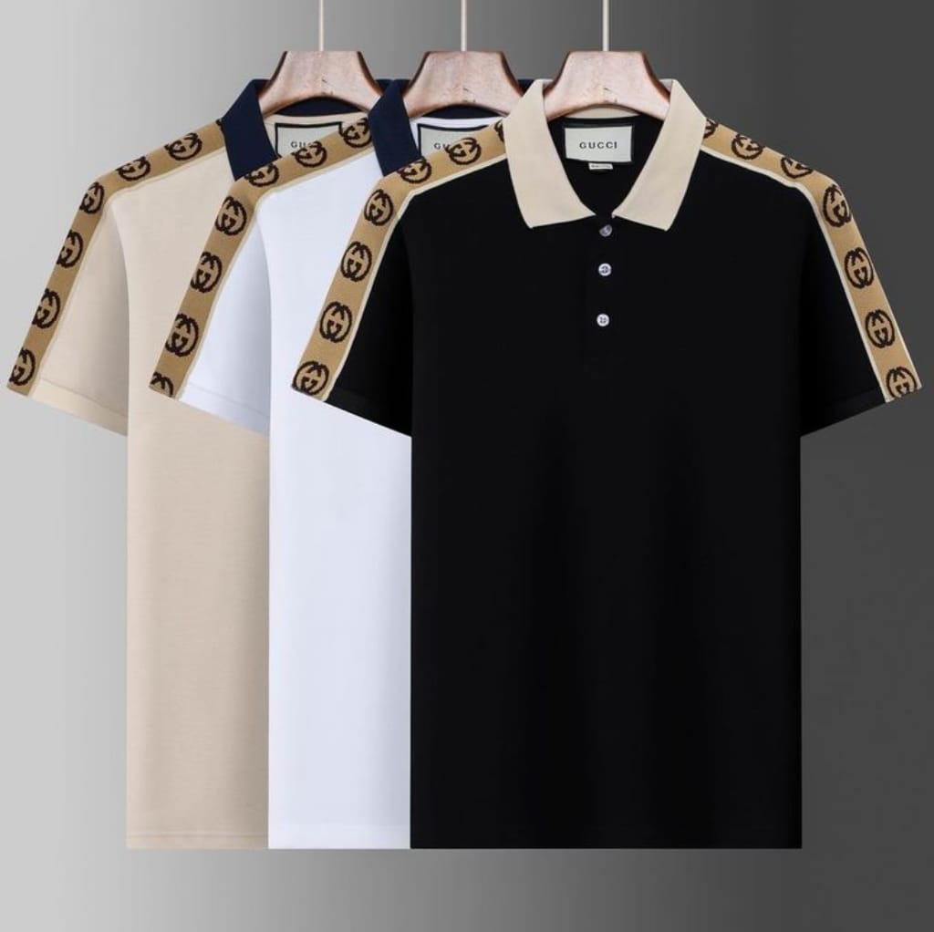 Three Gucci high-fashion polo shirts hanging on wooden hangers, featuring color-block designs with signature Gucci logo tape along the shoulders. The shirts are in beige, white, and black.