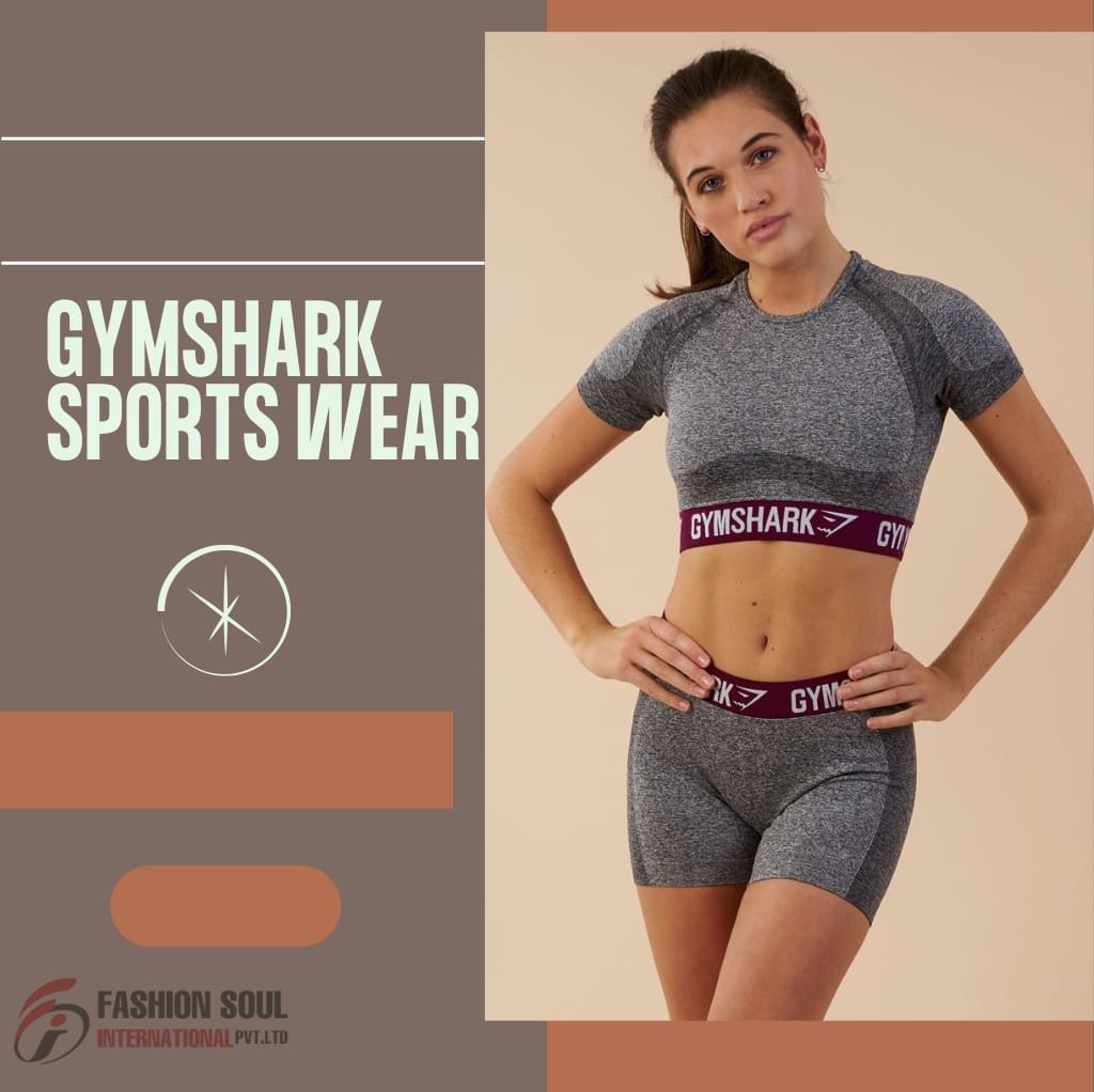 A young woman wearing grey Gymshark sportswear, including a crop top and shorts, standing with her hands on her hips against a neutral background. The text on the left side of the image reads "Gymshark Sports Wear," with additional branding from Fashion Soul International Pvt. Ltd. at the bottom.
