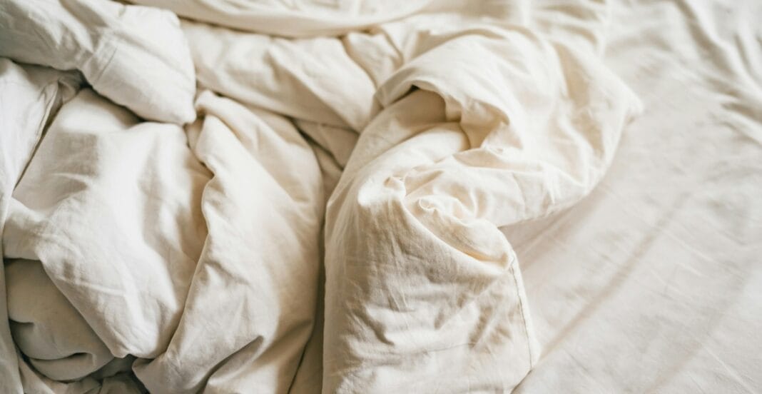 A messy, crumpled bed with white, rumpled bedding and sheets.