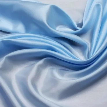 Close-up image of light blue satin-rayon spandex fabric with soft, flowing folds, showing its smooth, shiny surface.