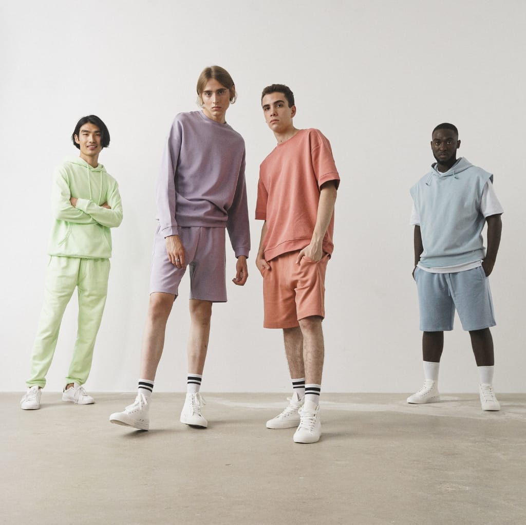A diverse group of four young adults dressed in colorful, casual streetwear outfits, standing against a plain white background.