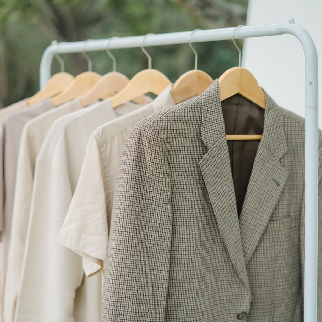Close-up of a checked blazer hanging on a wooden hanger on a clothing rack, with other neutral-colored garments in the background.