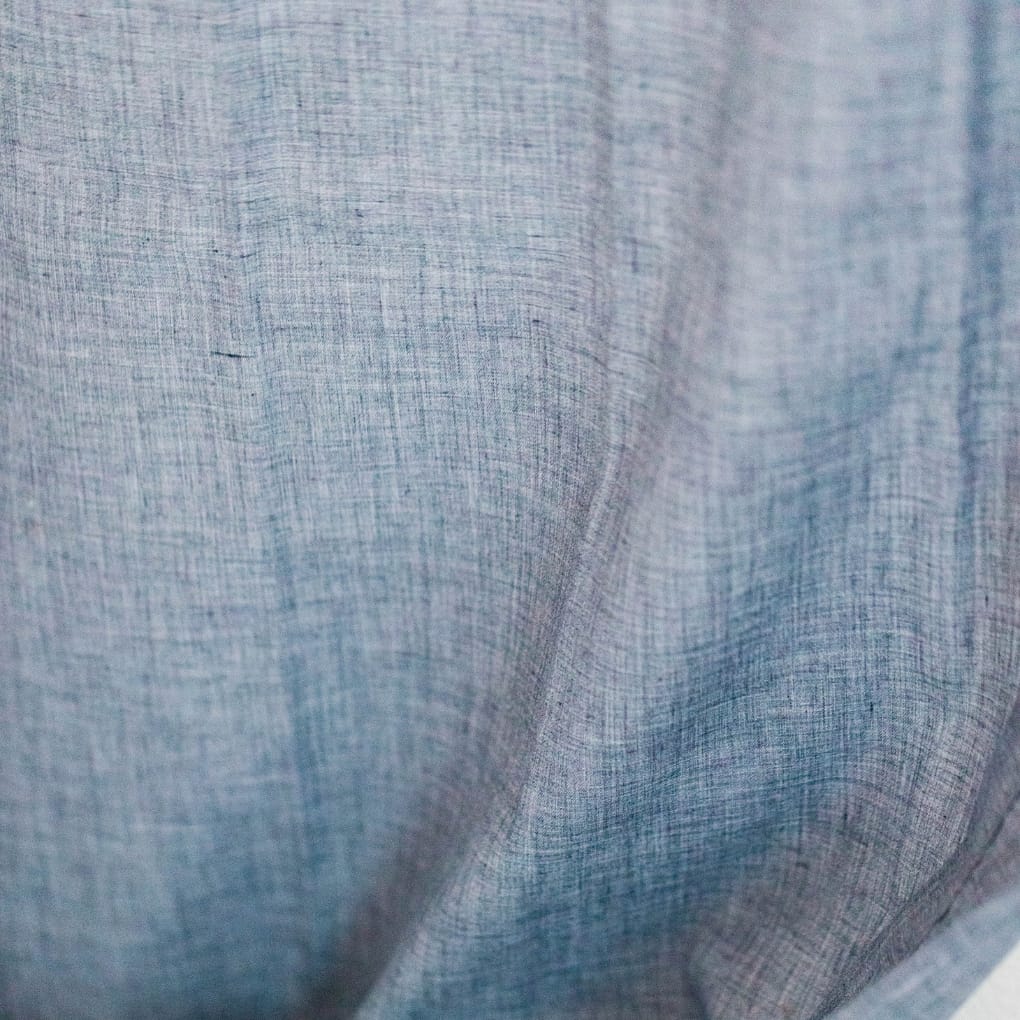 : Close-up of light blue fabric showing a finely woven, smooth texture with subtle variations, labeled "Chambray vs Denim."