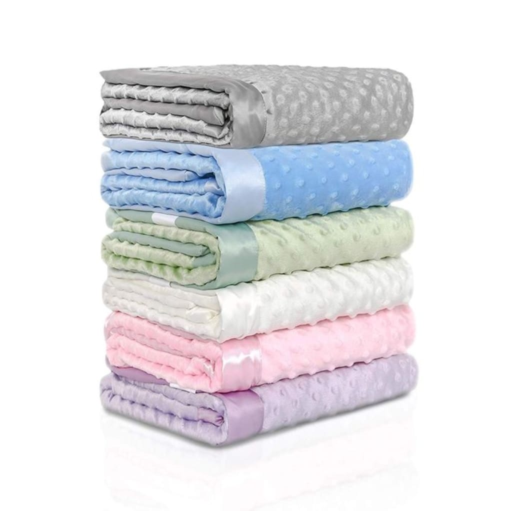 A neatly stacked pile of colorful, soft minky fabric blankets in shades of gray, blue, green, white, pink, and lavender, each with a textured, dotted surface.