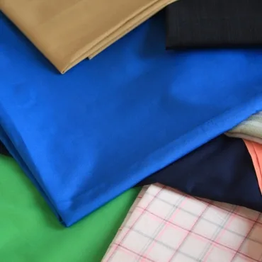 A stack of colorful rayon fabrics in beige, black, blue, navy, green, and pink plaid, neatly folded.