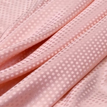 Close-up image of light pink jacquard spandex fabric with a dotted pattern and a smooth, shiny surface.