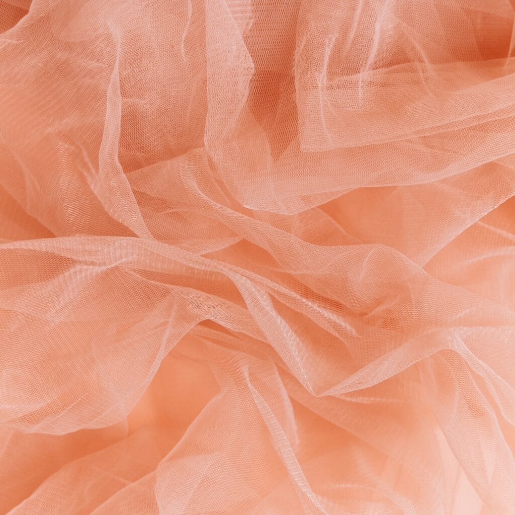 Close-up view of peach-colored tulle fabric with soft folds and a semi-transparent, mesh-like texture.