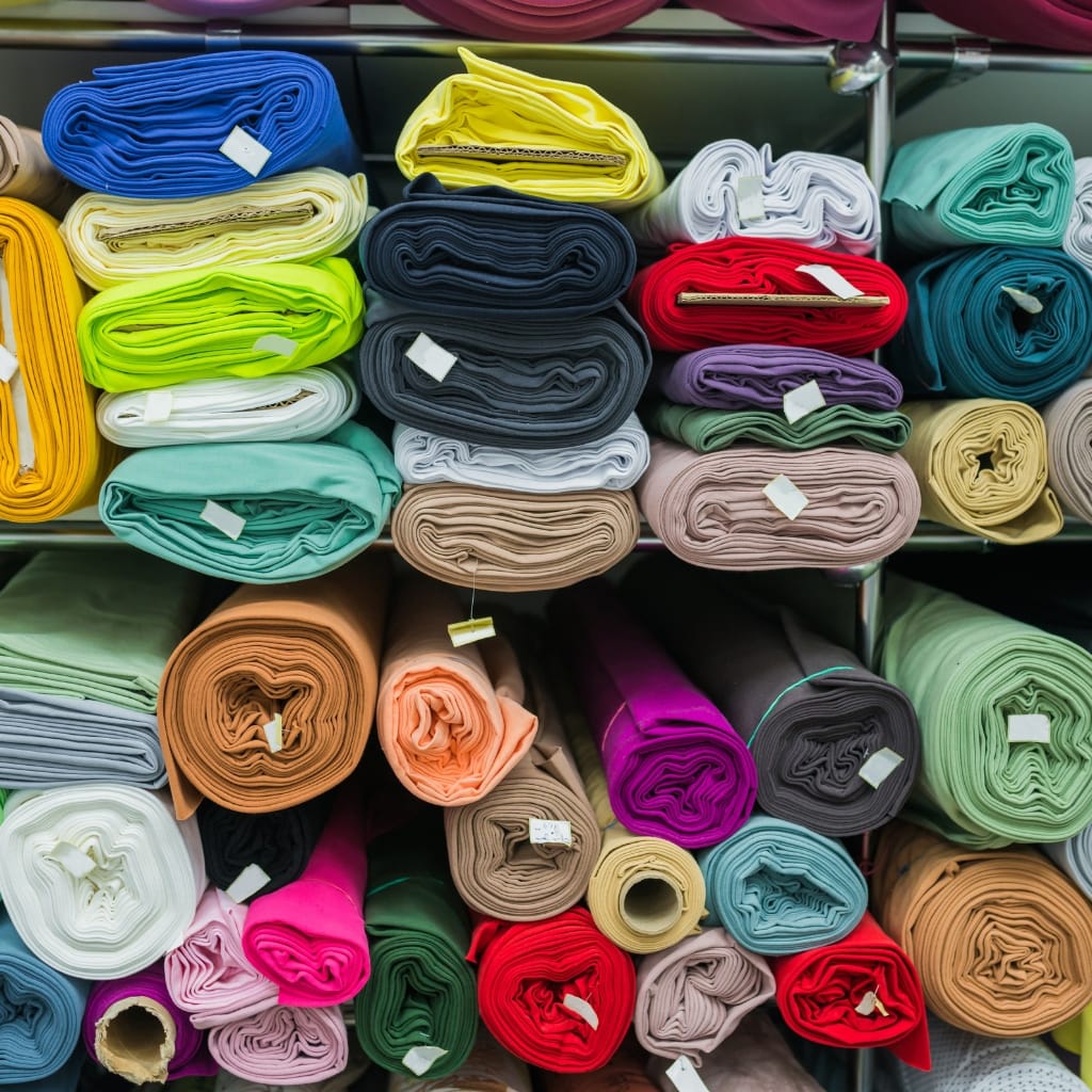 Rolls of fabric in various colors and sizes stacked on shelves, arranged in a colorful pattern.