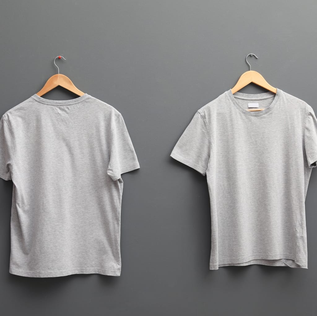 Two light gray T-shirts hanging on wooden hangers against a gray wall, with one T-shirt layered over the other to add visual depth.