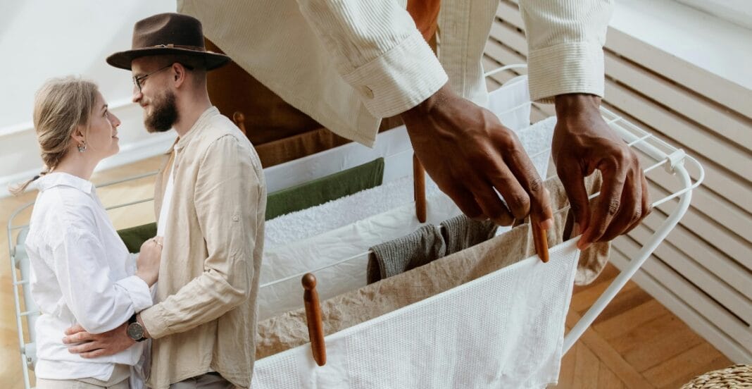 A person hanging laundry on a drying rack with a couple gazing lovingly at each other in the background.