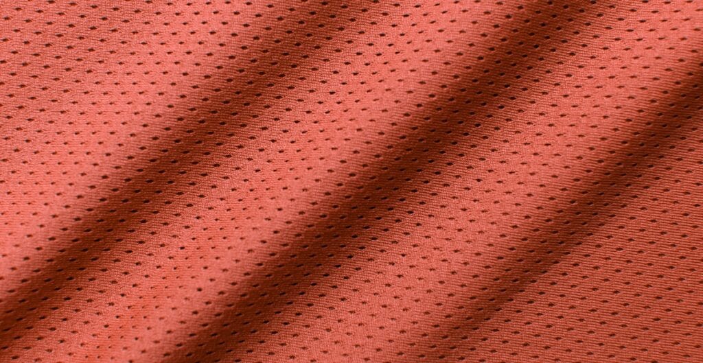 Close-up image of red mesh spandex fabric showing its perforated, breathable texture with small black dots.