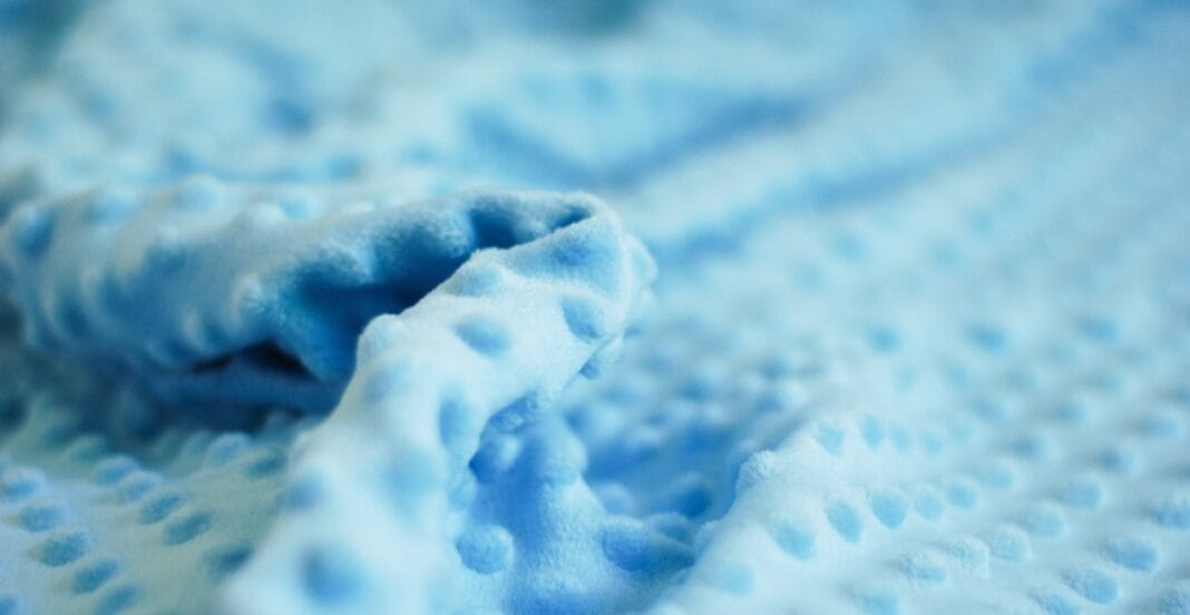 Soft, plush light blue fabric with a textured, dimpled surface and a rolled-up section in the foreground.