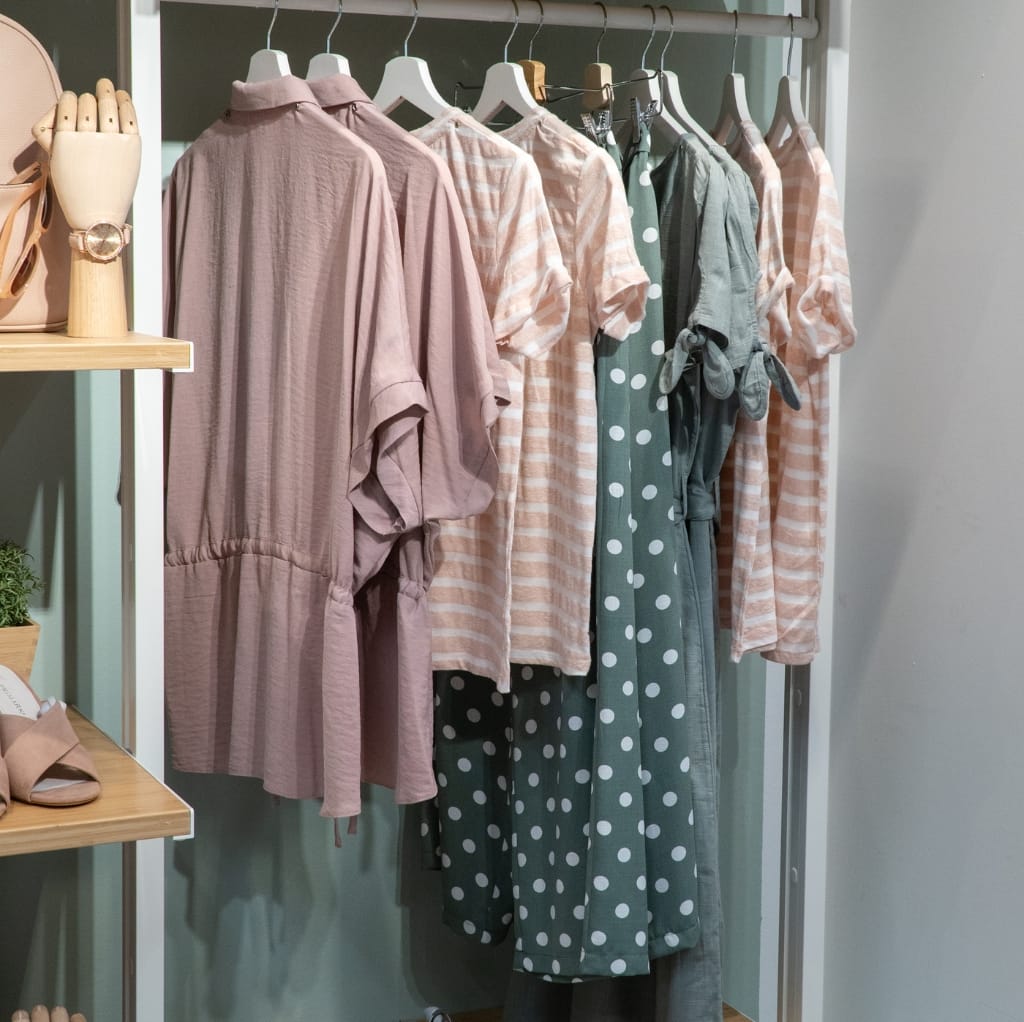 A display of various maxi cotton dresses hanging in a clothing store, featuring soft pastel and checkered patterns in shades of pink, green, and peach.