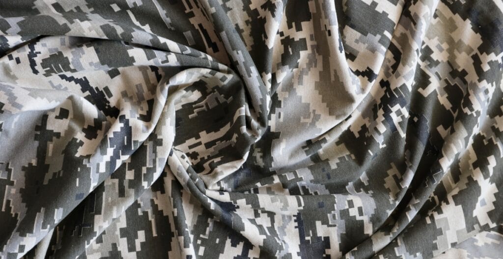 A piece of fabric with a digital camouflage pattern in shades of black, grey, and white, draped with soft folds and curves.