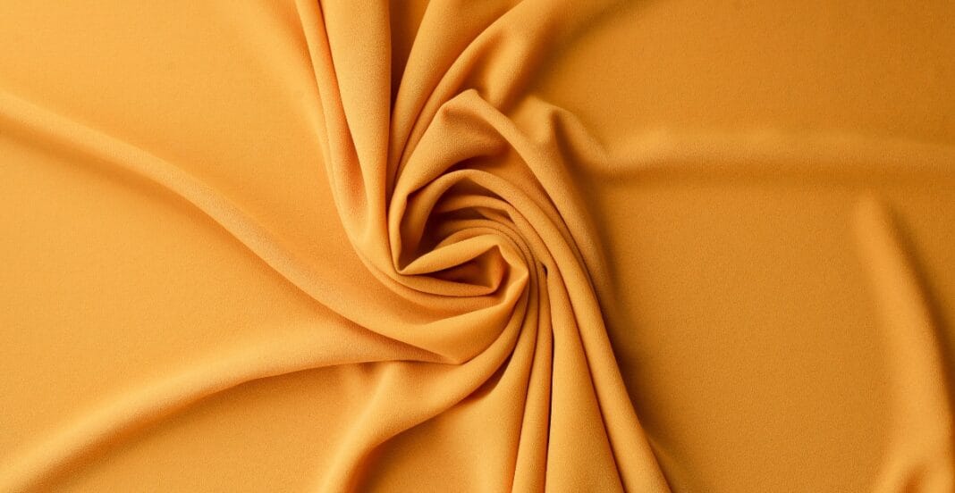 A close-up of folded, smooth, mustard-colored nylon spandex fabric with gentle drapes and a slight sheen.