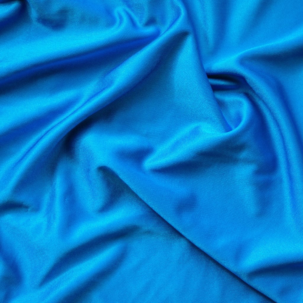 Close-up photograph of shiny, smooth, bright blue nylon spandex fabric with gentle folds and subtle sheen.