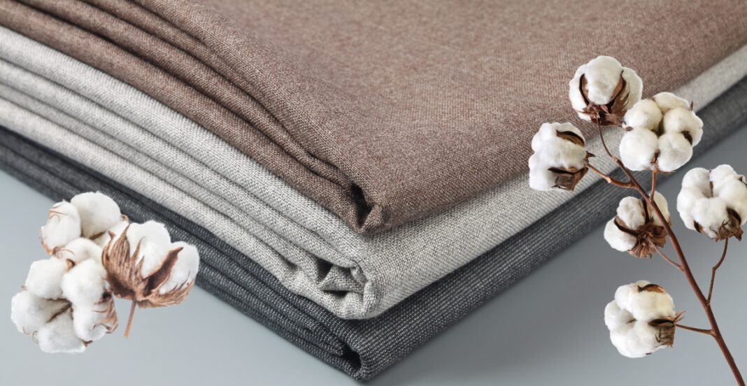 Three neatly folded pieces of fabric in shades of brown, beige, and gray with cotton branches placed beside them.