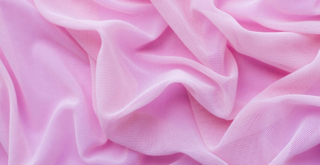 A close-up image of soft pink polyester organza fabric with delicate, lightweight, and semi-transparent texture, featuring tiny perforations.